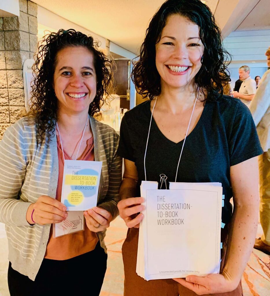 Katelyn and Allison holding a finished copy and manuscript copy of the Dissertation to Book Workbook