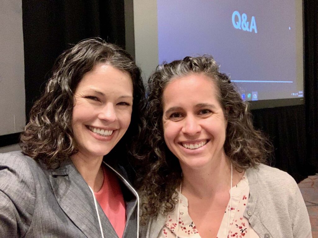 Allison and Katelyn together, smiling, with a conference presentation screen in the background